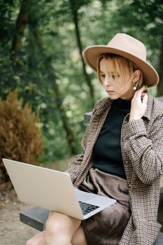 一名年轻女子戴着帽子，在户外用笔记本电脑工作，展现了远程工作的生活方式