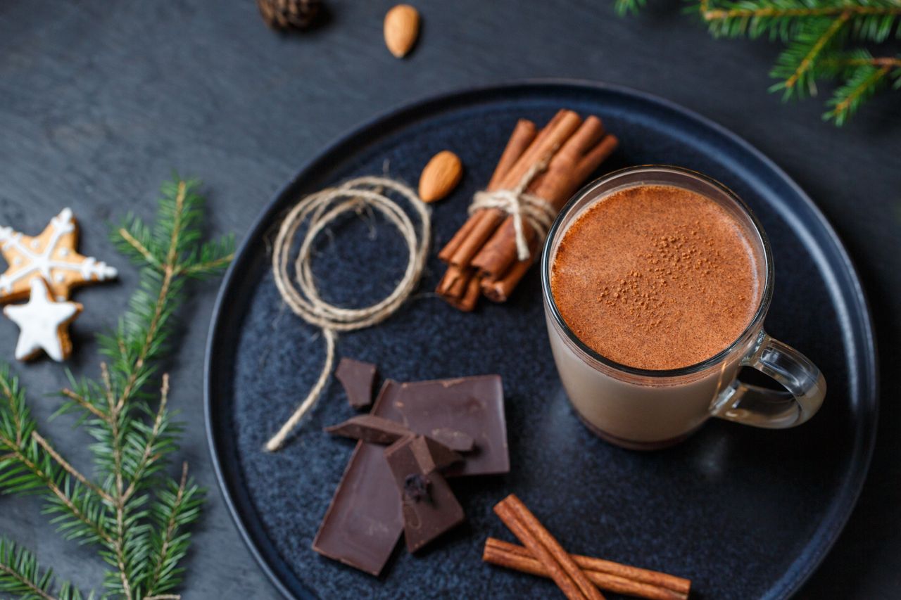 Glass of spiced cocoa surrounded by cinnamon sticks and dark chocolate
