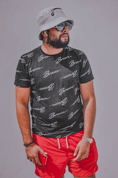 A fashionable man in casual attire with sunglasses, a bucket hat, and a smartphone.