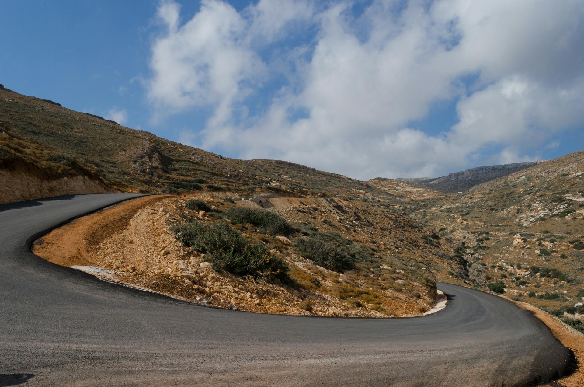 A winding mountain road in the remote landscape of Kythira, Greece under a bright sky.
