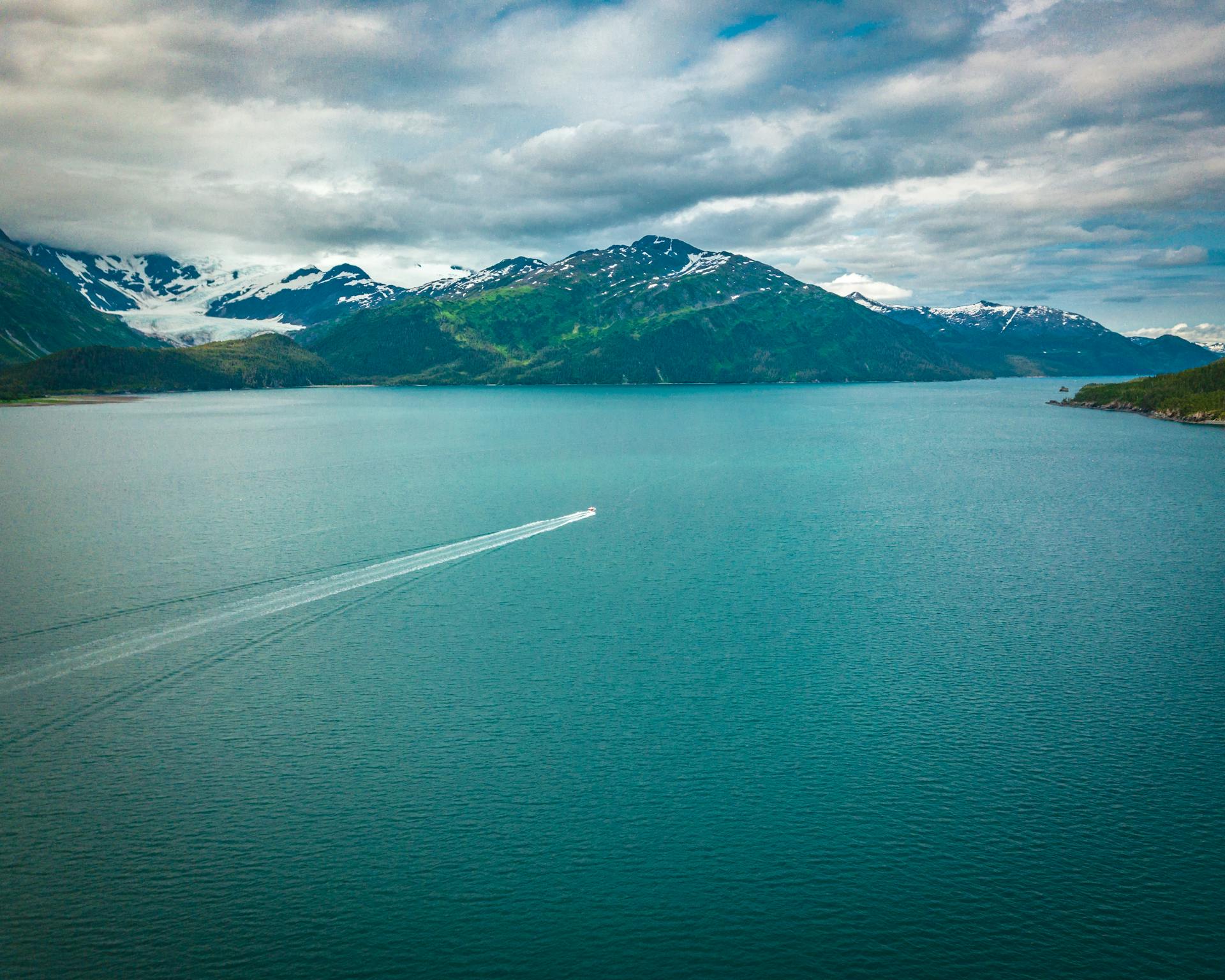 Scenic aerial view of a lone motorboat cruising on a vast Alaskan lake with mountains.