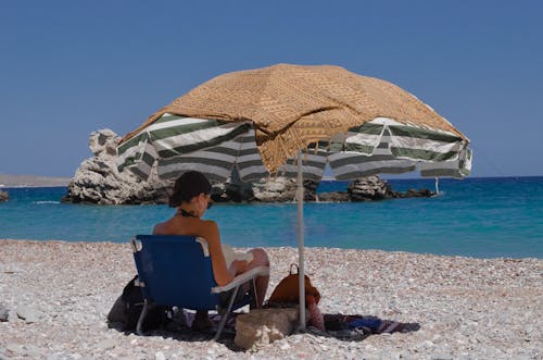 Free Woman Reading a Book under an Umbrella on a Beach Stock Photo