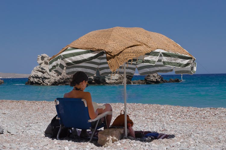 Woman Reading A Book Under An Umbrella On A Beach