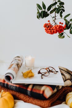 温暖的秋天，配有蜡烛、眼镜、摊开的书和鲜艳的罗望子，非常适合营造舒适的秋季氛围