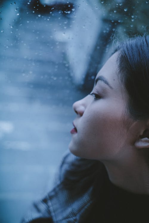 Calm teen girl looking through wet window in rainy day