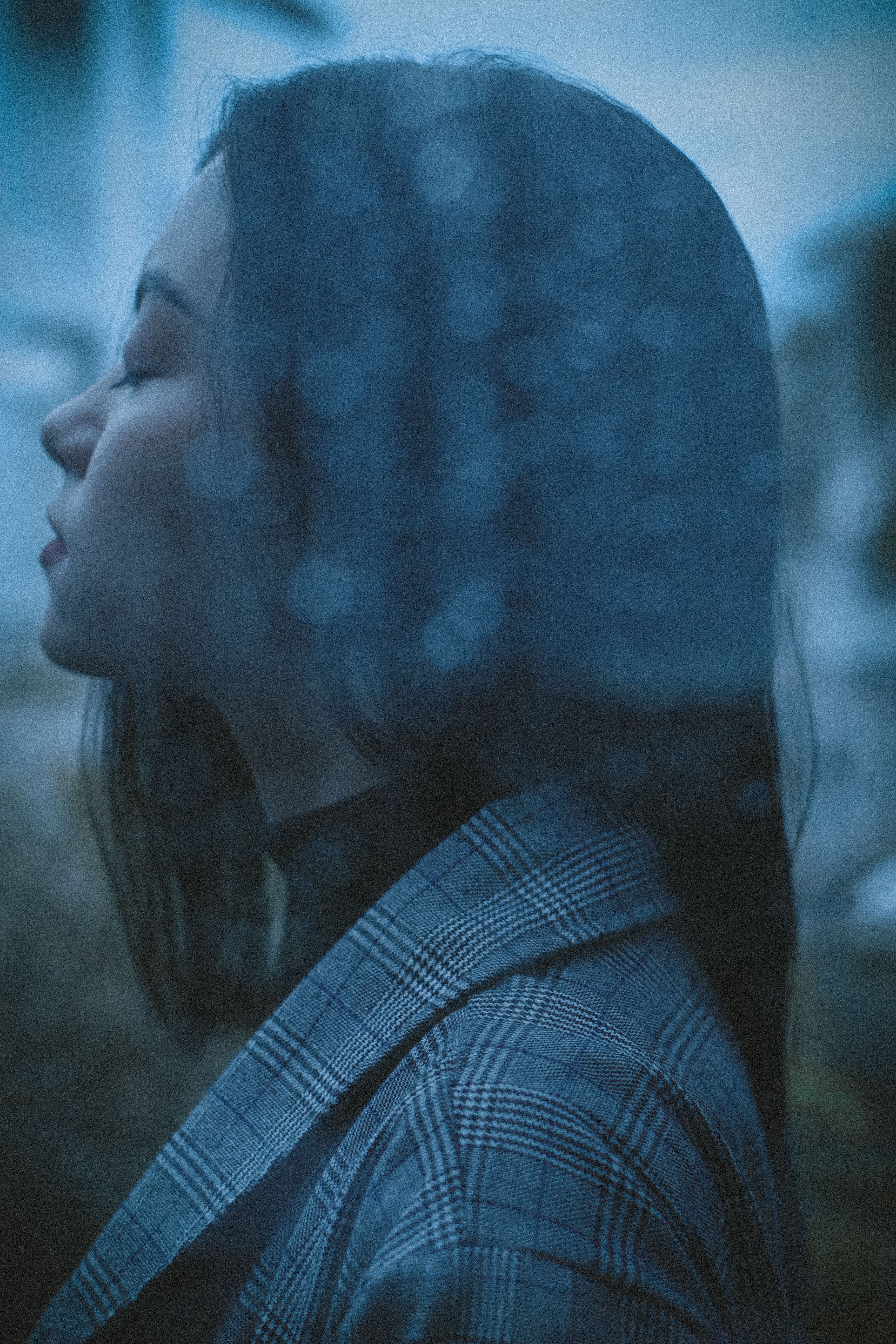 透过玻璃侧面图，一位心烦意乱的少女闭着眼睛，站在雨天潮湿的窗户后面