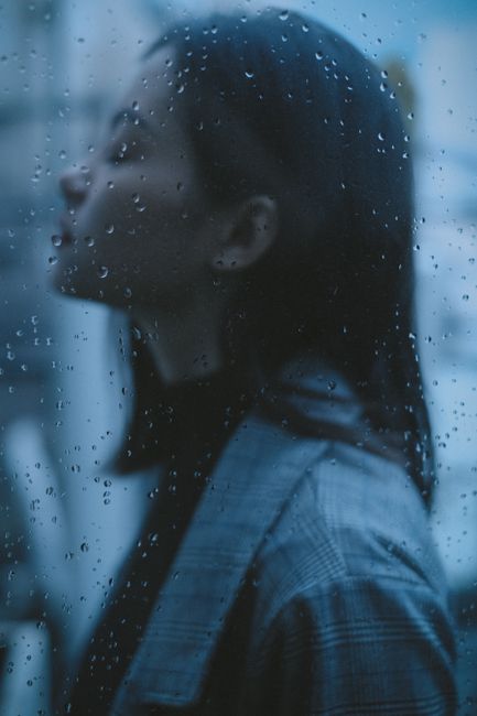 Through glass side view of pensive teen with closed eyes thinking in gloomy rainy day