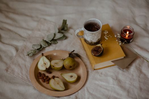 Warm still life with pears, a cup, candle, and book on a rustic fabric.