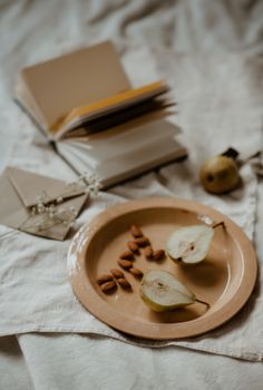 这是一幅以切片的梨、杏仁和一本打开的书为特色的乡村静物作品，营造出舒适的氛围