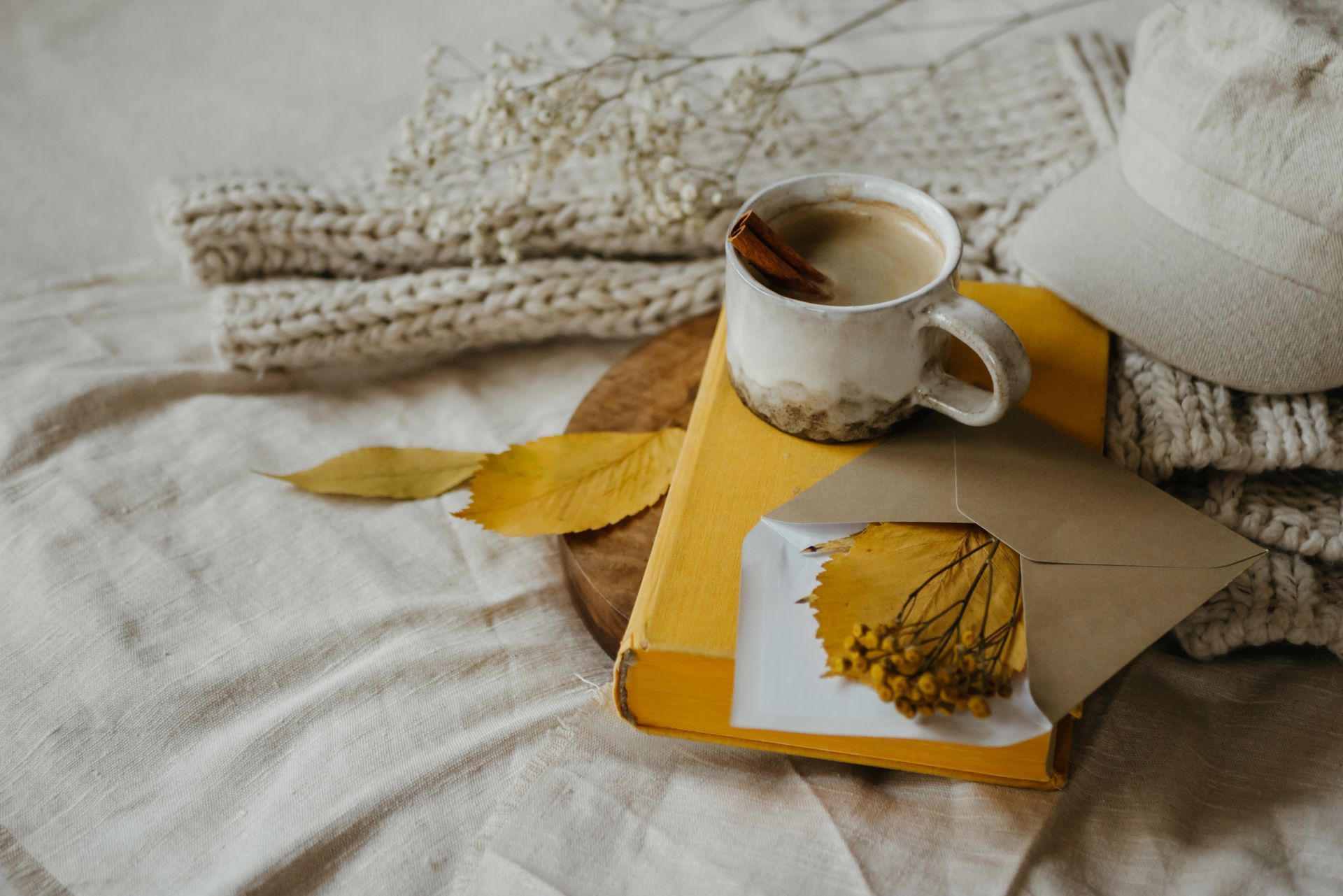 Warm and inviting autumn scene featuring a ceramic mug of coffee with cinnamon, knitted sweater, and fall leaves.