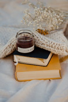 Warm autumn-themed still life with a candle, books, knitted scarf, and flowers.