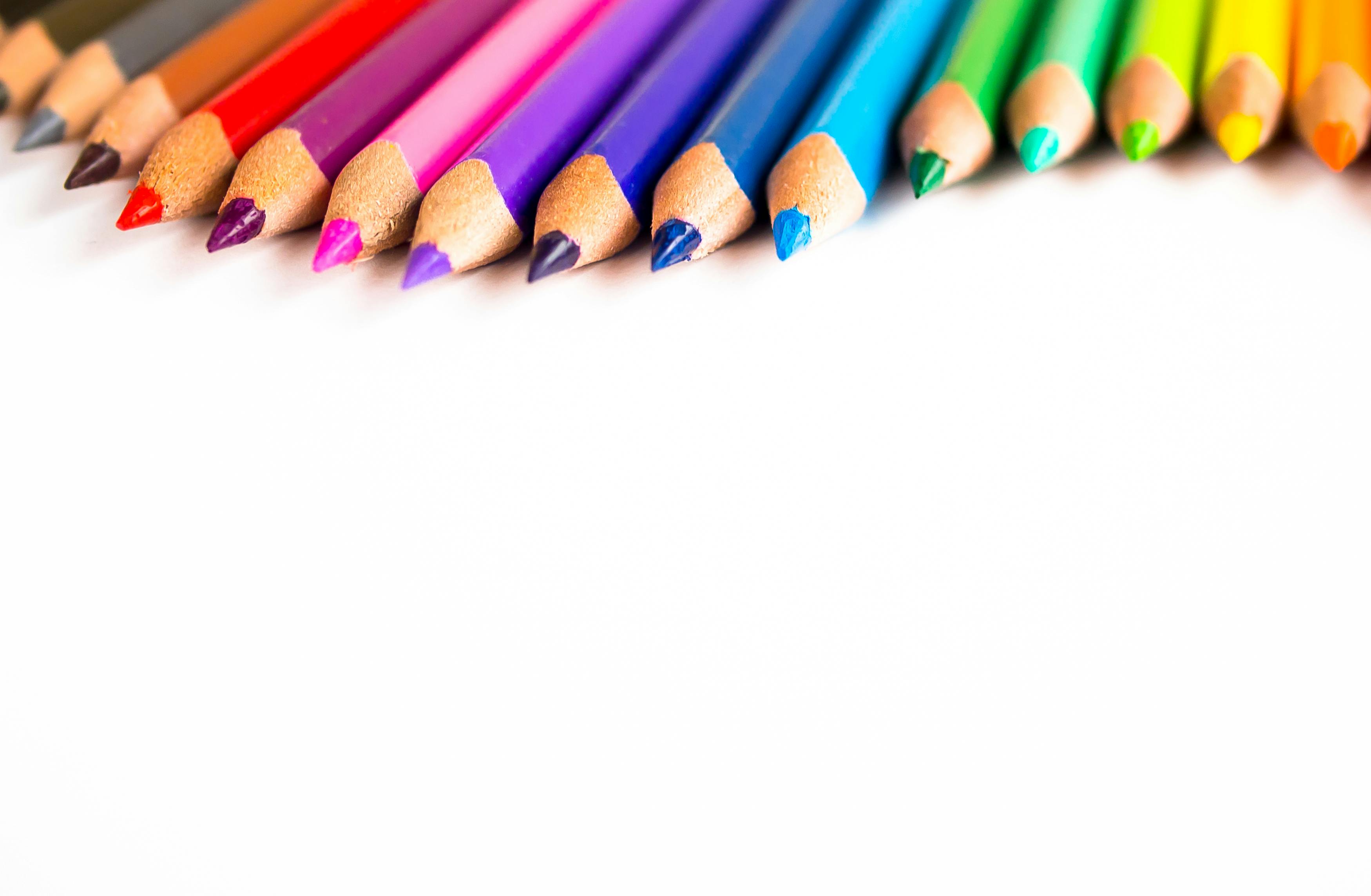 白色表面上排列着彩色铅笔的特写镜头，提供了充满活力的复印空间