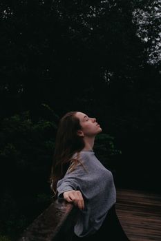 一位棕色长发、闭着眼睛的宁静女性侧身站在公园栏杆上
