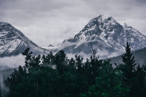 Free Majestic snow-covered mountains captured in the Canadian Rockies, featuring lush greenery and clouds. Stock Photo