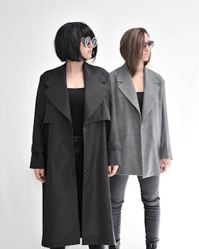 Young stylish women in contemporary clothes and sunglasses standing on white background while looking away