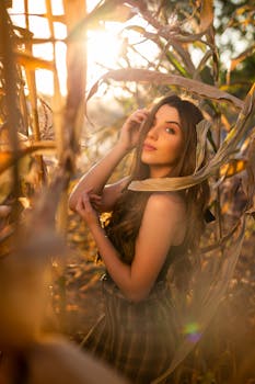 A beautiful young woman poses in a sunlit cornfield, capturing a serene and natural moment.