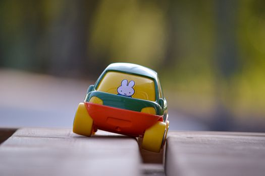 Vibrant toy car with rabbit sticker in soft focus, captured on wooden plank outdoors.
