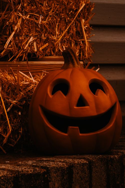 Free Spooky jack o lantern decoration for halloween party placed near wooden wall with hay in dark barn during celebration of autumn holiday Stock Photo