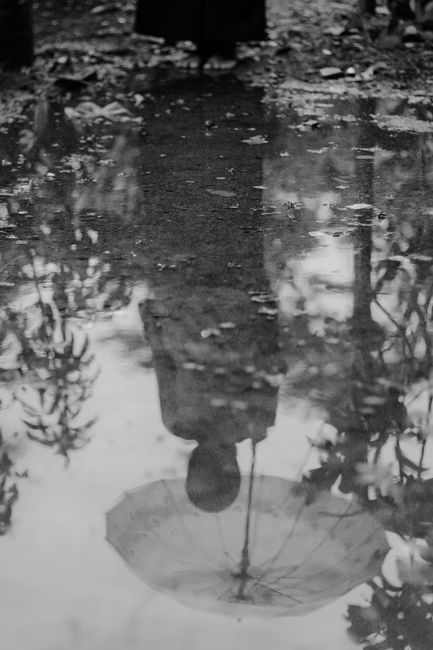 Moody black and white reflection of a person with umbrella in a puddle.