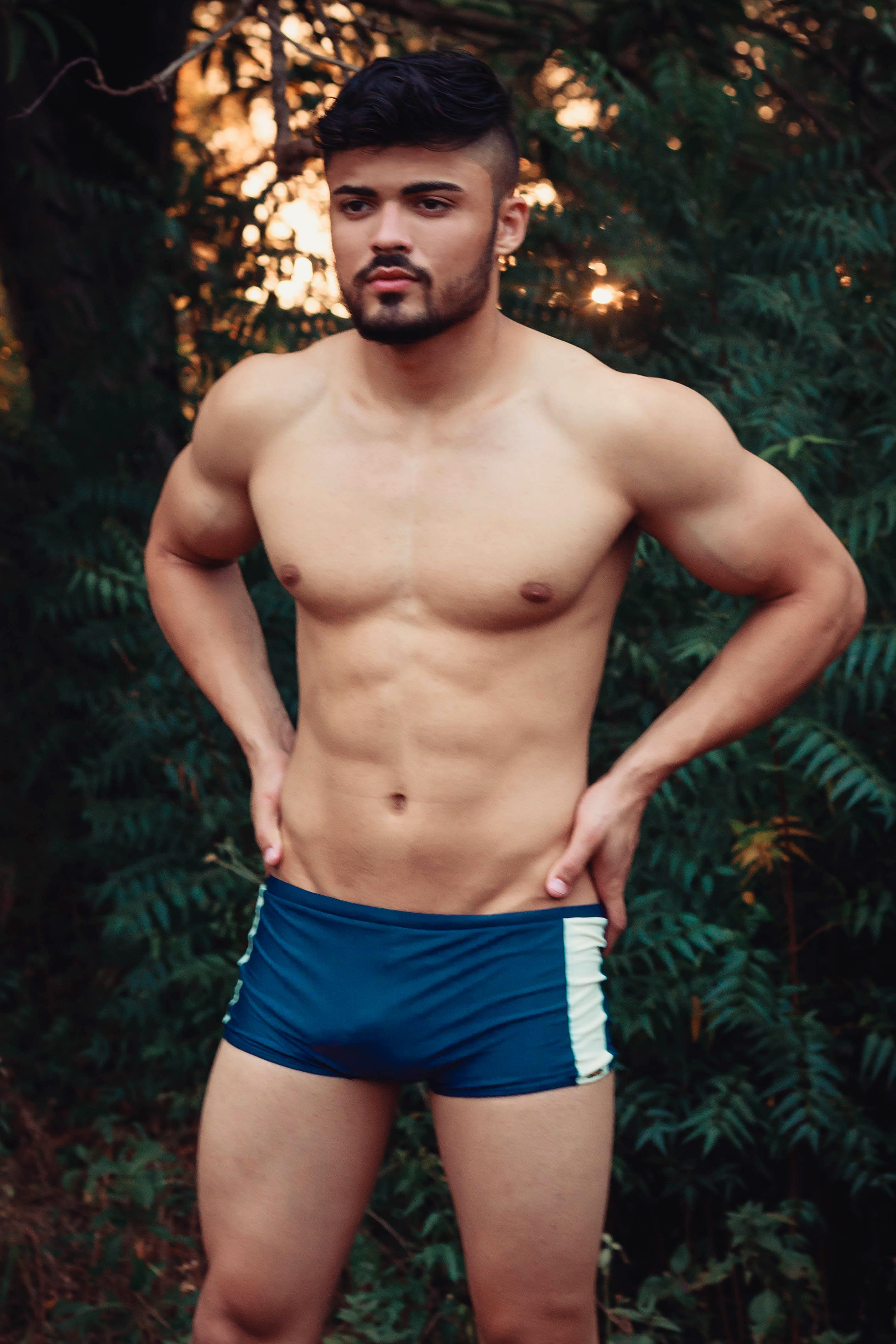 Homem musculoso sem camisa com olhar pensativo na natureza, incorporando fitness e tranquilidade.