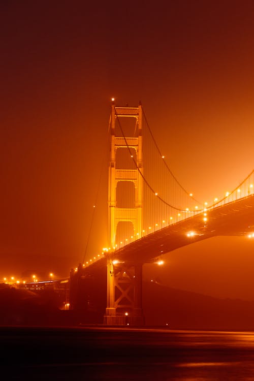 Golden Gate Bridge illuminated with street lights and crossing calm water in foggy weather at night