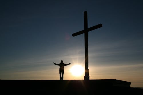 Gratis Siluet Orang Yang Berdiri Di Samping Salib Saat Matahari Terbenam Foto Stok