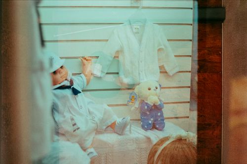 Free Storefront display featuring a cute doll, teddy bear, and baby clothes in soft colors. Stock Photo