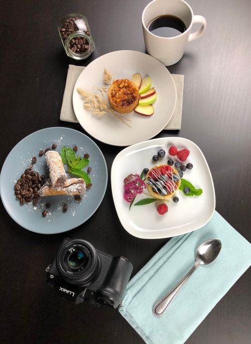 Free Flat lay of assorted desserts and coffee on a dark table with camera and cutlery. Stock Photo