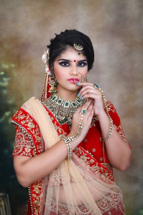 Free Serious young Indian woman in sari and red traditional clothes with necklace and piercing with earrings and makeup while looking at camera Stock Photo