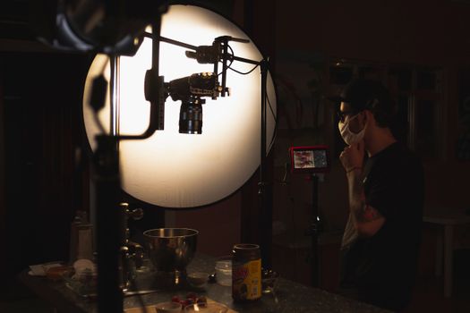 Photographer adjusts camera in well-lit studio. Visible equipment and light setup.