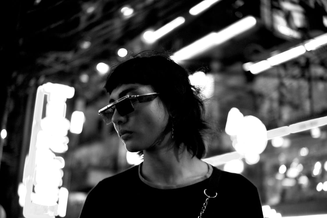 Black and white of serious androgynous Asian man in sunglasses standing on street