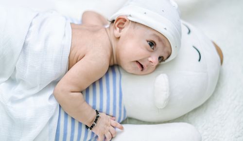Free From above back view of crop adorable infant in baby cap lying on toy while looking away in house Stock Photo