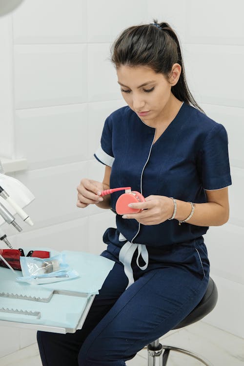 Concentrated young female doctor with toothbrush and denture sitting on chair in dentist office