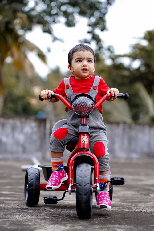 Free Adorable child on a red tricycle enjoying a sunny day outdoors. Stock Photo