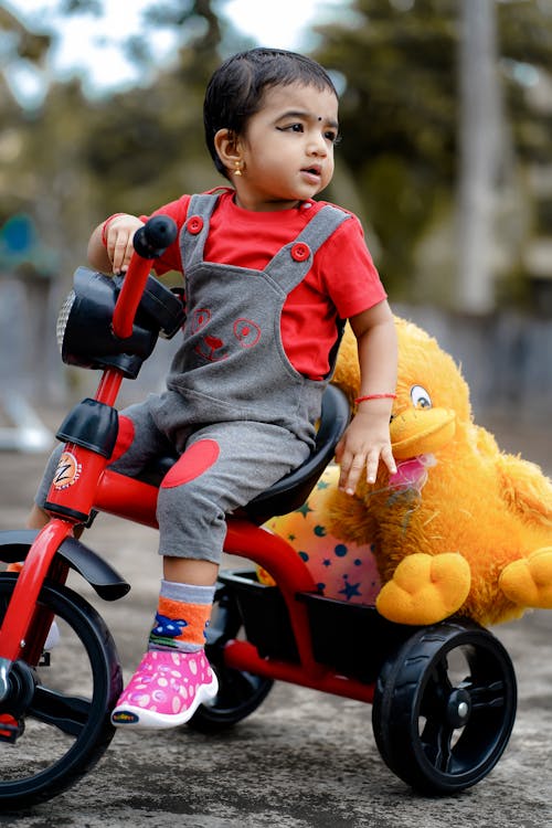 Free Cute Child riding a Bike Toy carrying Stuffed Toys Stock Photo