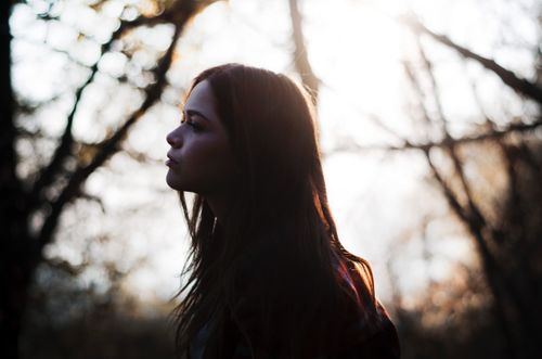 Free Silhouette of a woman in a forest with sunlight filtering through the trees. Stock Photo