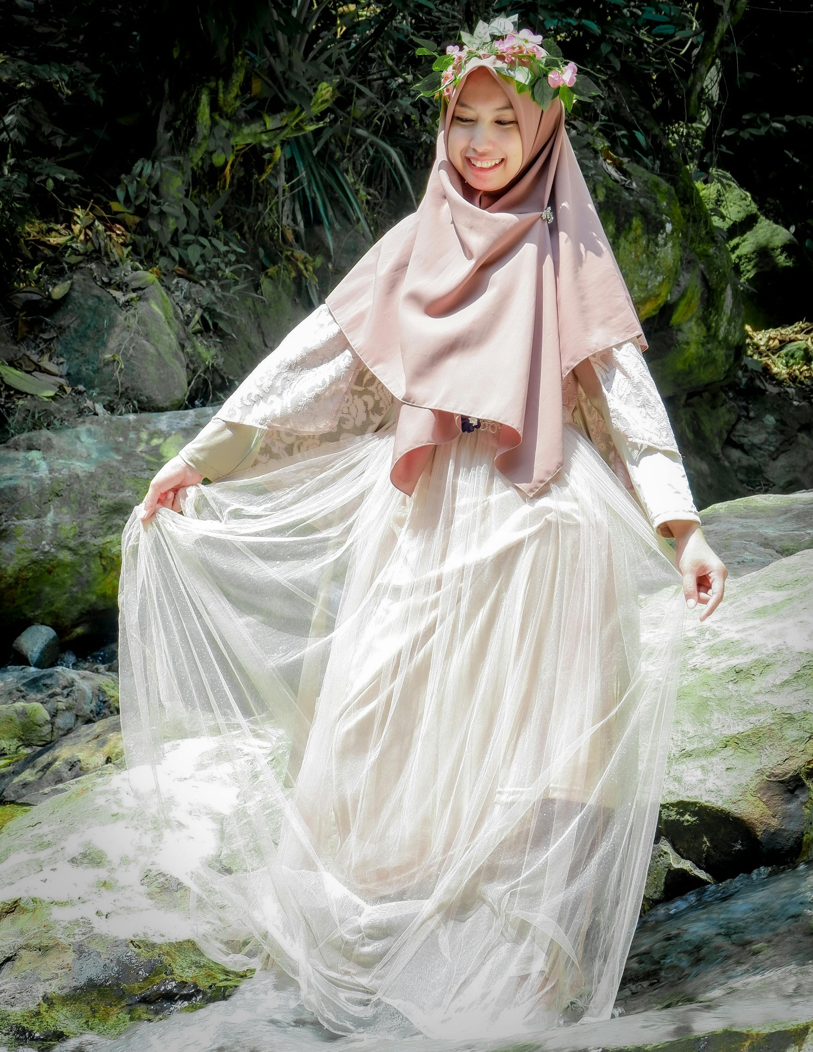 Beautiful woman wearing hijab and sheer dress, smiling in nature.