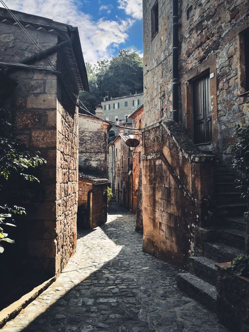 Free A picturesque cobblestone alley lined with old stone buildings under a blue sky. Stock Photo