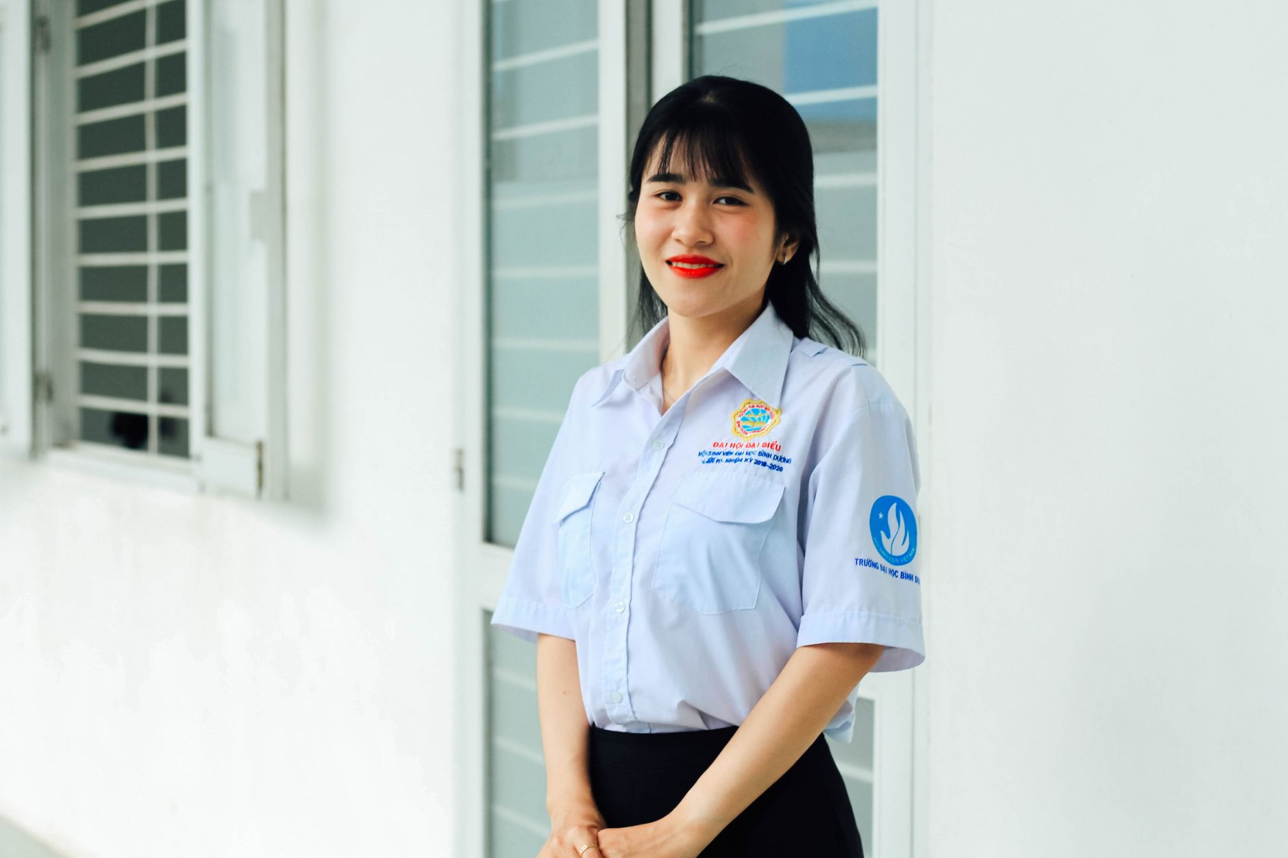 Asian woman in uniform smiling indoors near windows, displaying confidence and warmth.
