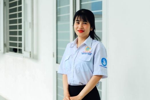 Asian woman in uniform smiling indoors near windows, displaying confidence and warmth.