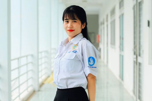 Asian woman in school uniform smiling indoors, showcasing confidence and positivity.