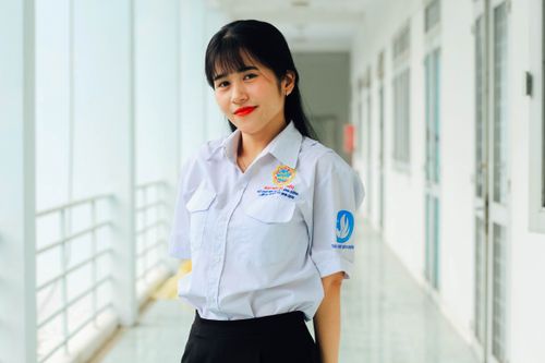 Free Asian woman in a white button-up shirt smiling in an indoor hallway setting. Stock Photo