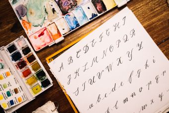 Practice sheet of script letterforms next to a watercolour palette — photo by Anna Tarazevich on Pexels