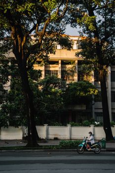 一辆摩托车飞驰过一栋绿树成荫的建筑，捕捉到了城市生活的瞬间