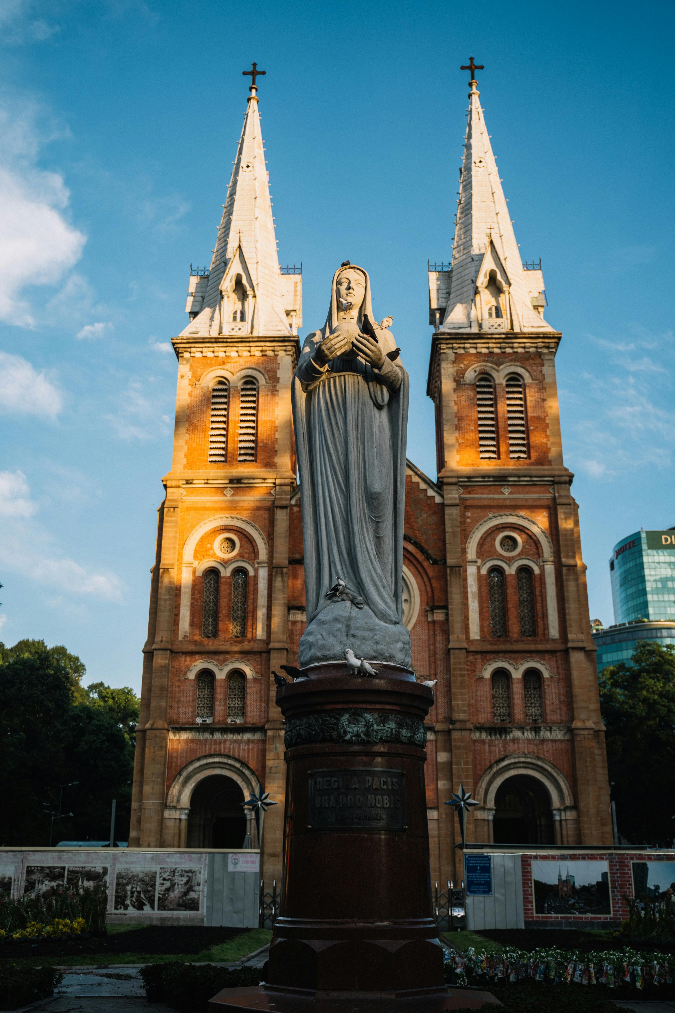 从低角度仰望蓝天下的圣母玛利亚雕像，背景是大教堂的尖顶