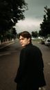 Back view of serious male in elegant black suit walking on asphalt path and looking over shoulder