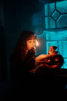 在一间光线昏暗的蓝色房间里，一名妇女点燃了一盏雕刻的南瓜灯