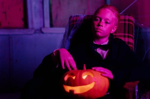 A Boy Sitting on a Chair while Holding a Jack O Lantern on His Lap