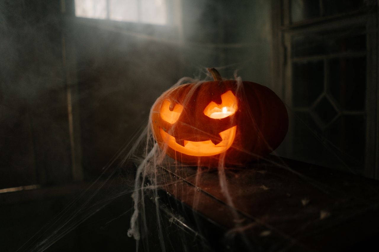 carved pumpkin jack o lantern illuminated on a spooky cobwebbed indoor