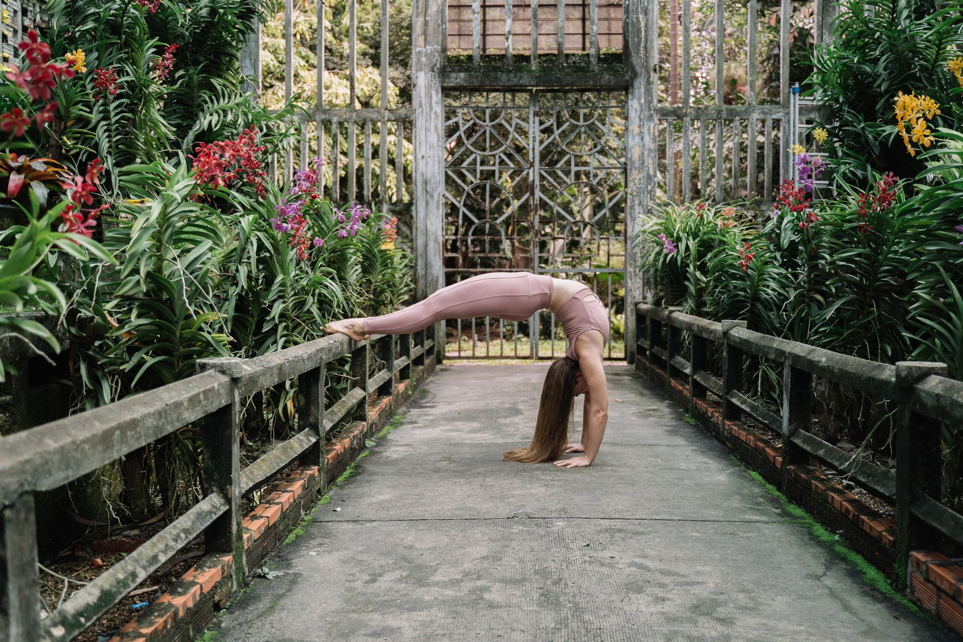瑜珈墊選擇對頸椎腰椎有影響嗎?選購指南助你避開傷害 A woman in a backbend yoga pose surrounded by vibrant flowers in a serene outdoor garden.